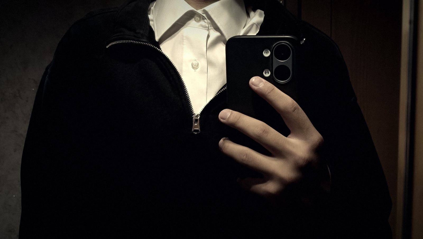 Schwarzer Pullover mit Zipper über weißem Hemd, Smartphone in der Hand